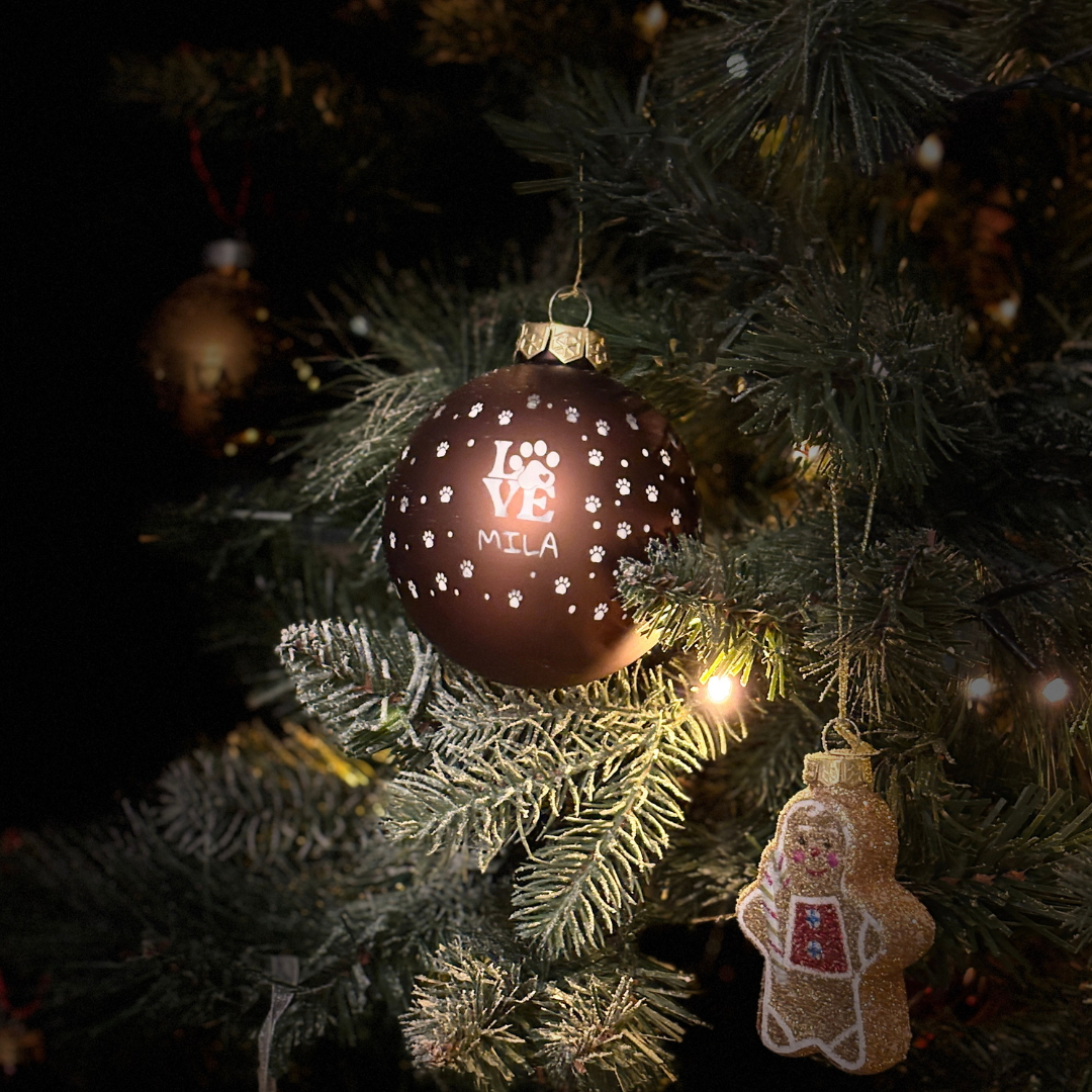 Gepersonaliseerde kerstbal met naam voor hond of kat, hangend aan een kerstboom, warm en feestelijk.